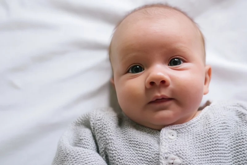 Baby lying on white blanket wearing gray knitted onesie