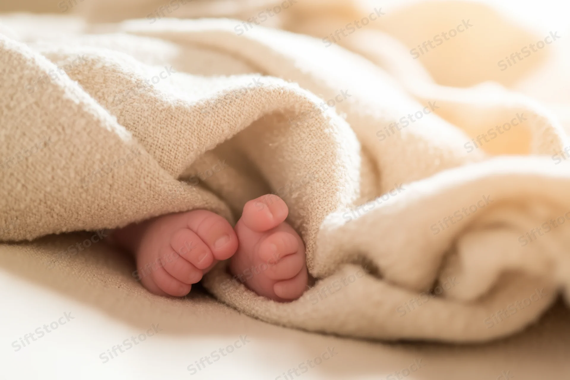 Newborn baby's tiny feet peeking from beneath a soft knitted blanket in a cozy setting