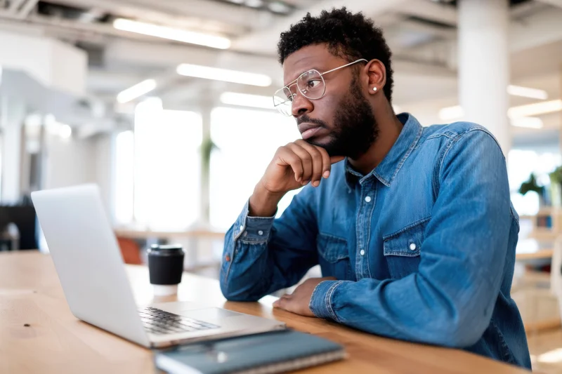 Man in denim shirt concentrating at laptop in modern office workspace