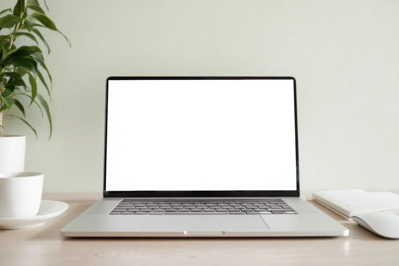Open laptop with blank white screen on a minimalist desk beside a plant and coffee cup
