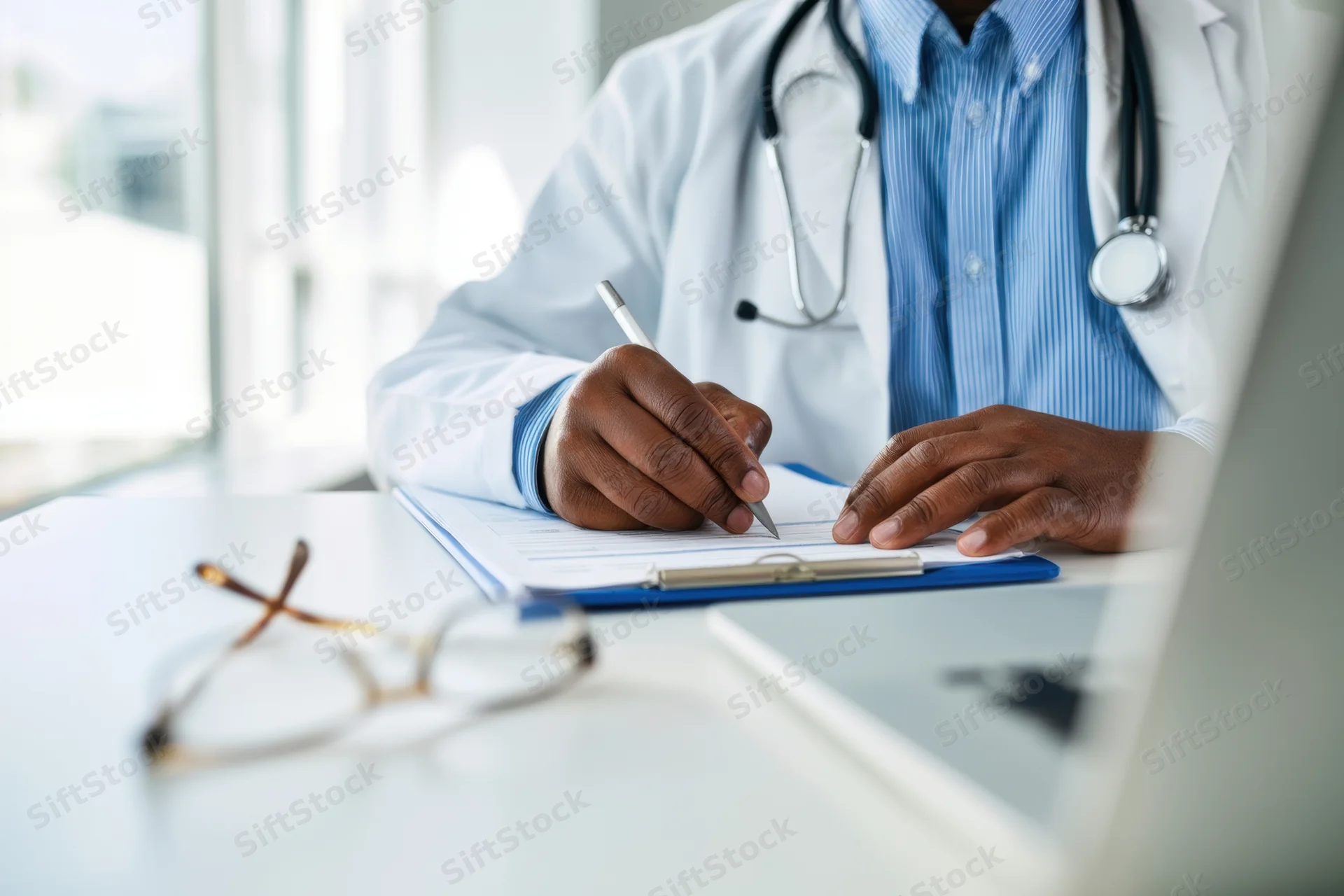 Doctor writing notes on a clipboard at a desk in an office