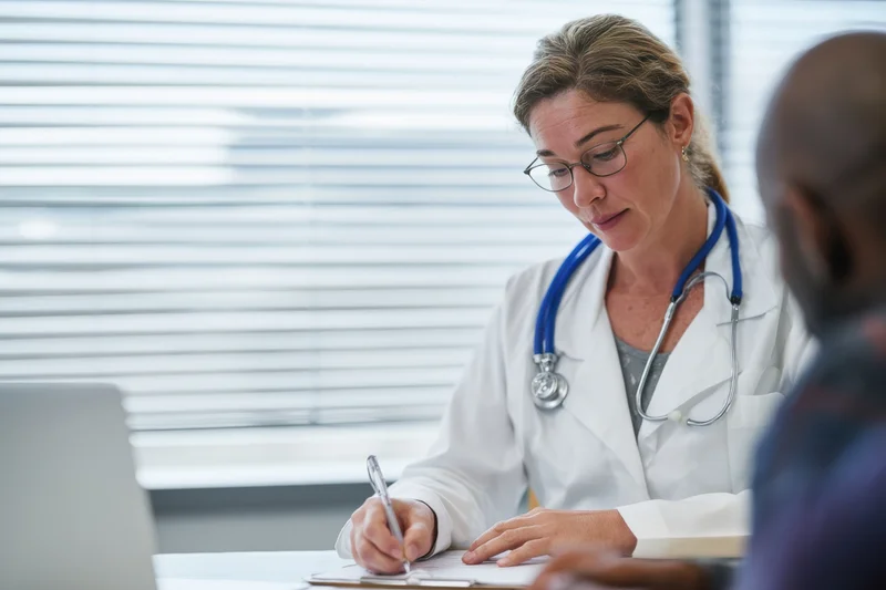 Female doctor writing on clipboard during patient consultation in clinic office