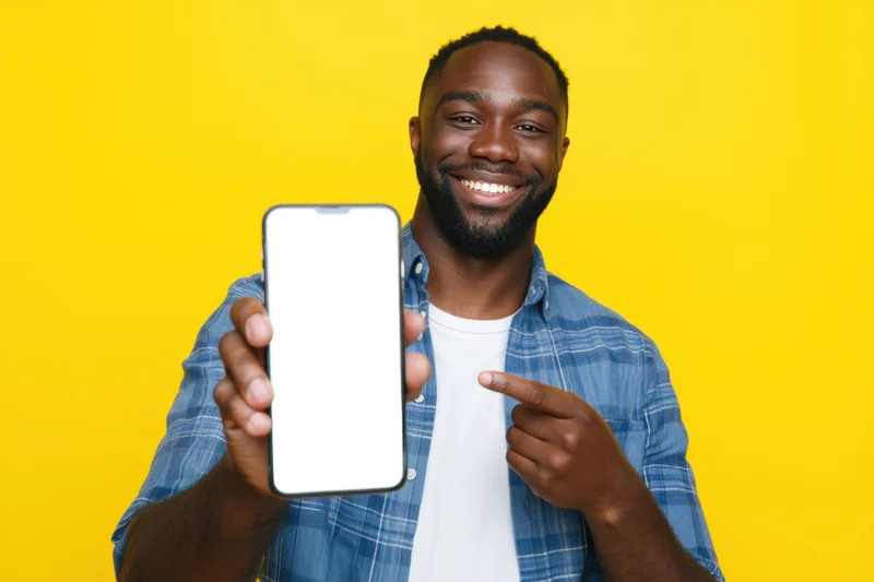 Smiling man pointing at smartphone screen against yellow background