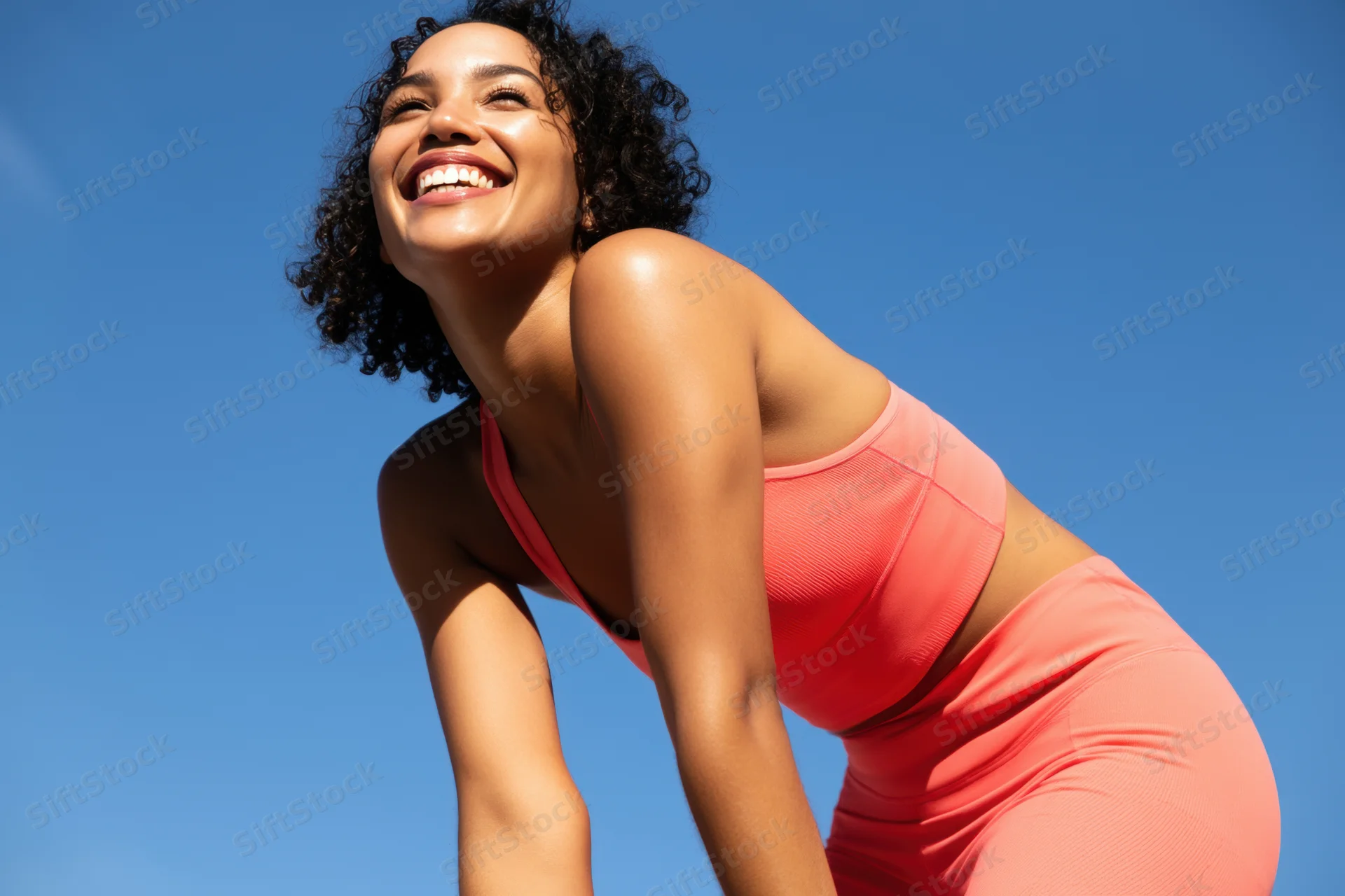Woman in coral athletic outfit leaning forward outdoors smiling under blue sky