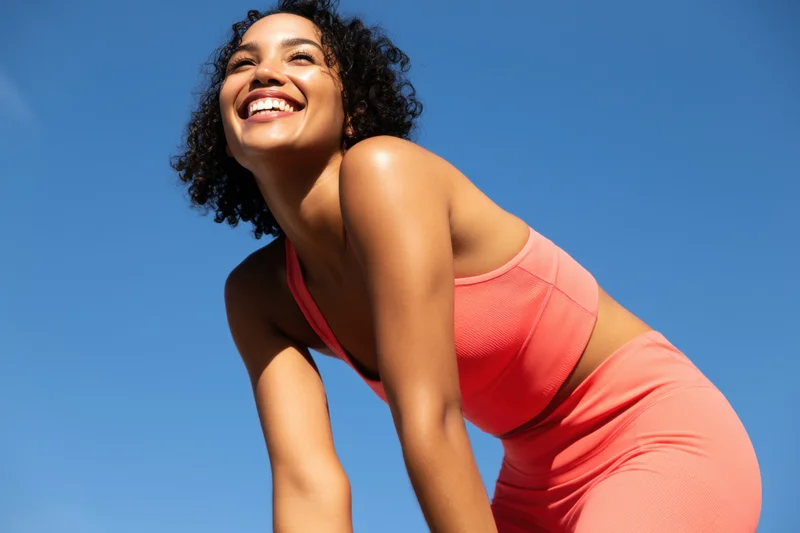 Woman in coral athletic outfit leaning forward outdoors smiling under blue sky