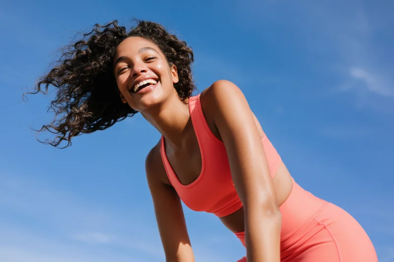 Joyful woman in coral athletic outfit leaning forward outdoors under blue sky