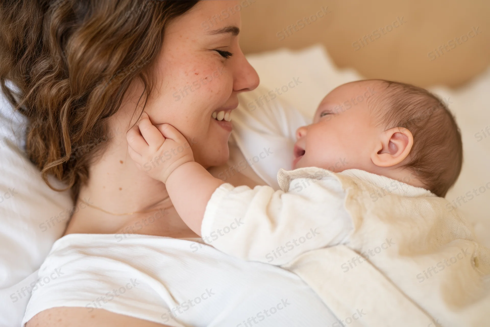 Mother smiling at her baby lying close on a bed