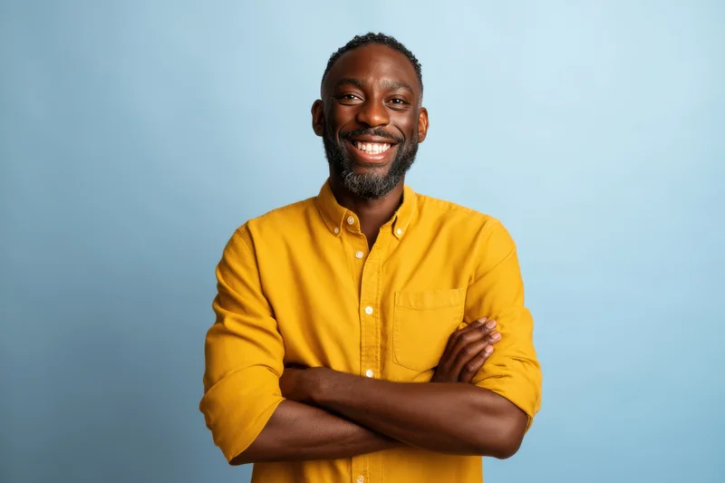 Smiling man with arms crossed wearing yellow shirt against light blue background