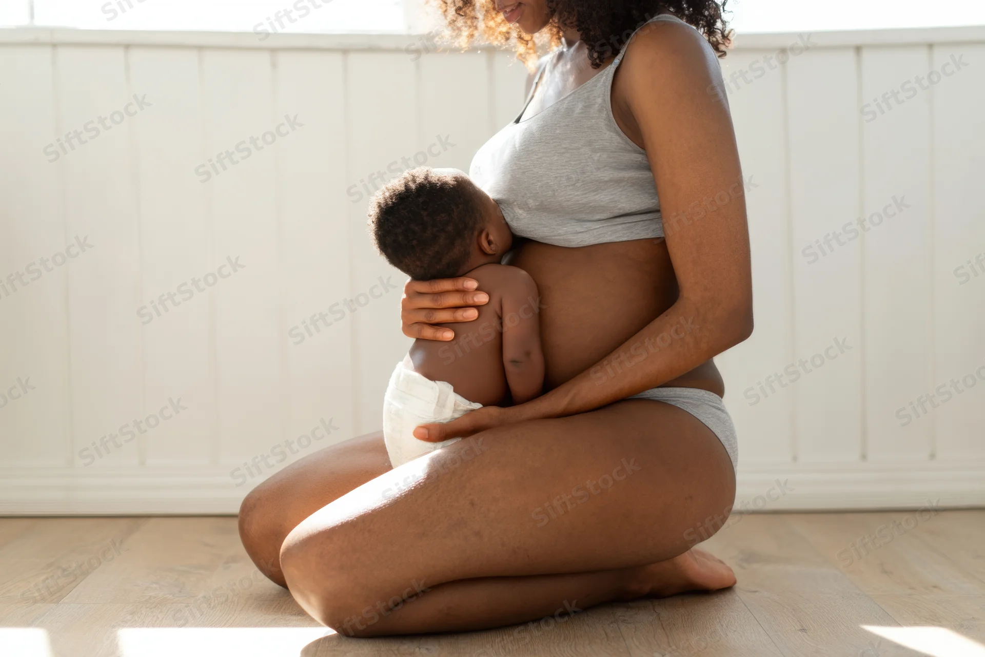 Mother breastfeeding baby while kneeling on wooden floor indoors