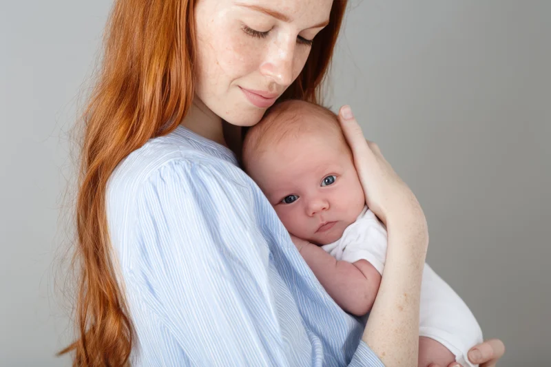 Mother holding newborn baby close to her chest in a studio portrait