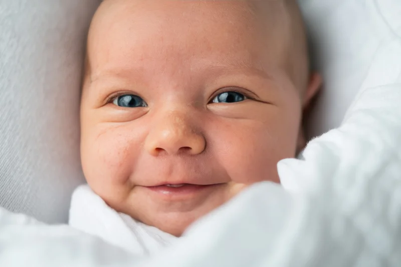 Closeup of a smiling newborn baby lying on a soft white blanket