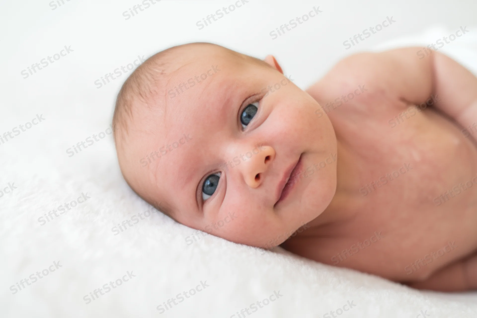 Newborn baby lying on a white blanket with blue eyes and a gentle smile