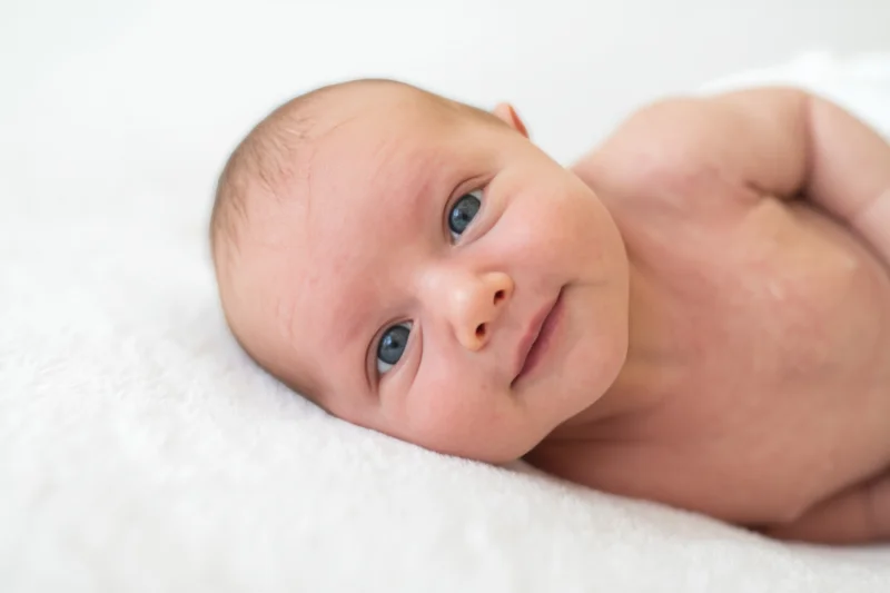 Newborn baby lying on a white blanket with blue eyes and a gentle smile