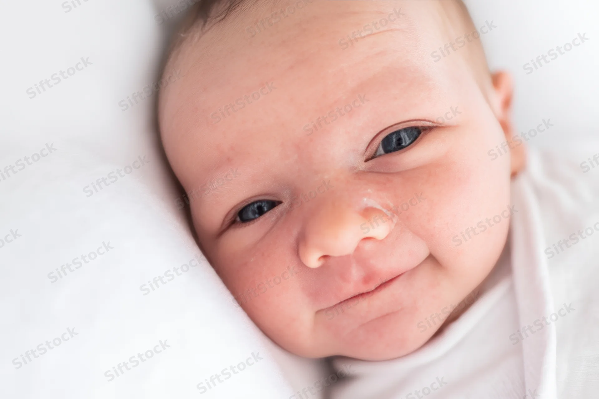 Newborn baby smiling with blue eyes wrapped in white blanket