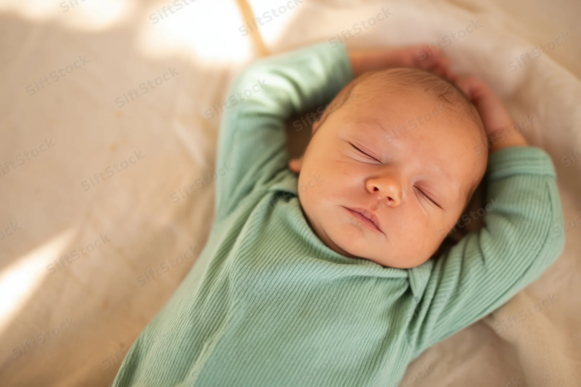 Newborn baby sleeping peacefully with arms above head on soft blanket in natural light