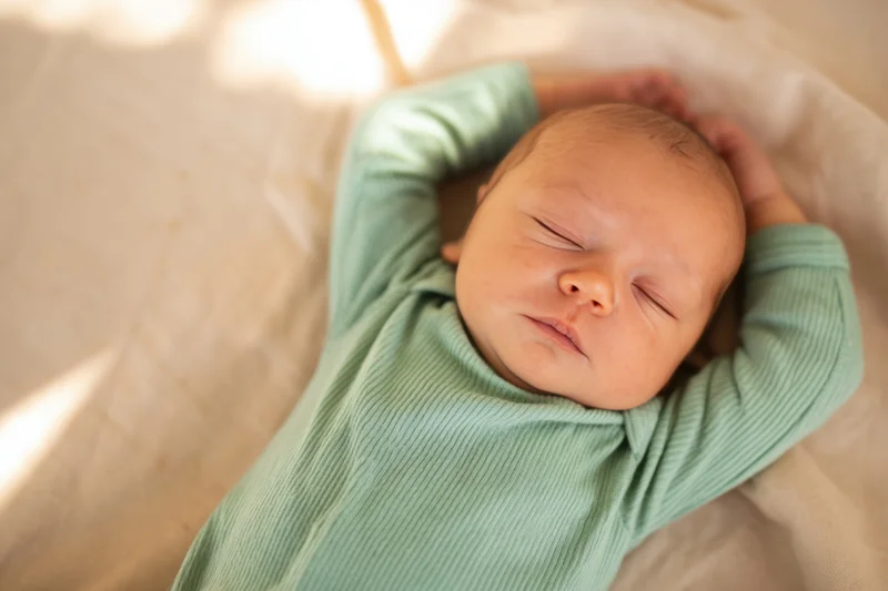 Newborn baby sleeping peacefully with arms above head on soft blanket in natural light