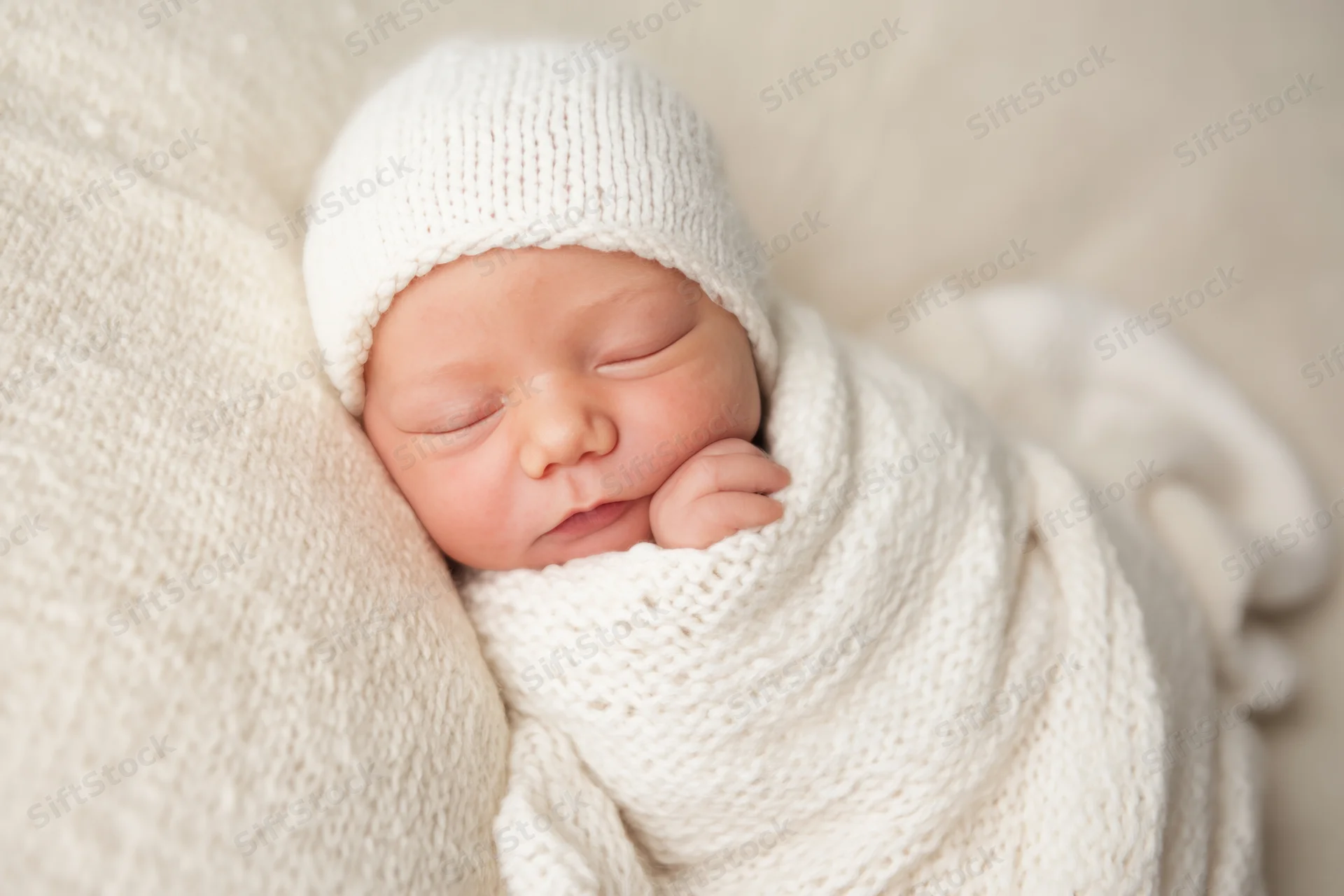 Newborn baby sleeping peacefully wrapped in cream knitted blanket and hat