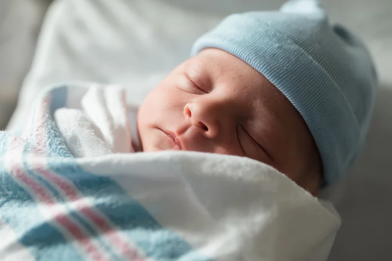 Newborn baby sleeping peacefully swaddled in a white blanket with blue hat
