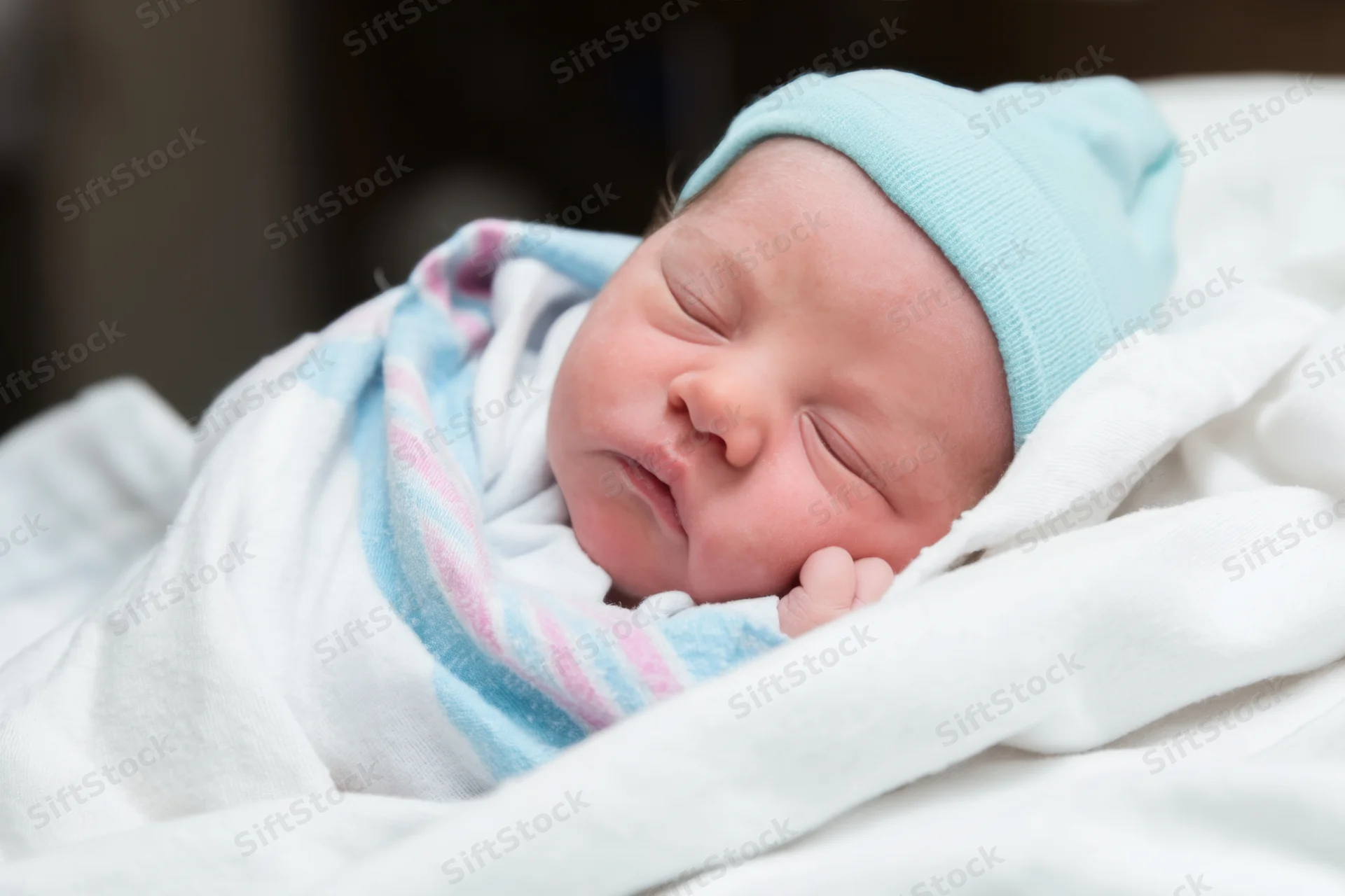 Newborn baby sleeping peacefully swaddled in a white blanket with a blue hat