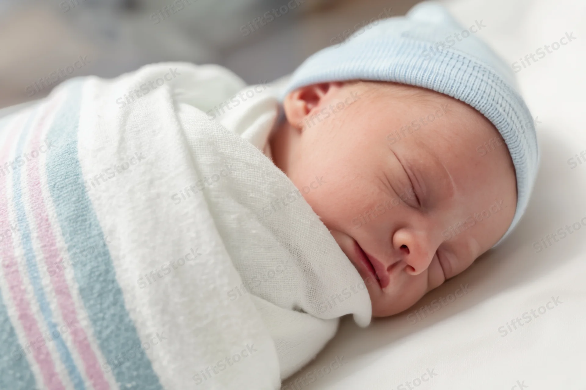 Newborn baby sleeping peacefully swaddled in a white blanket with blue hat