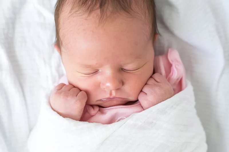 Newborn baby sleeping swaddled in a white blanket with pink clothing