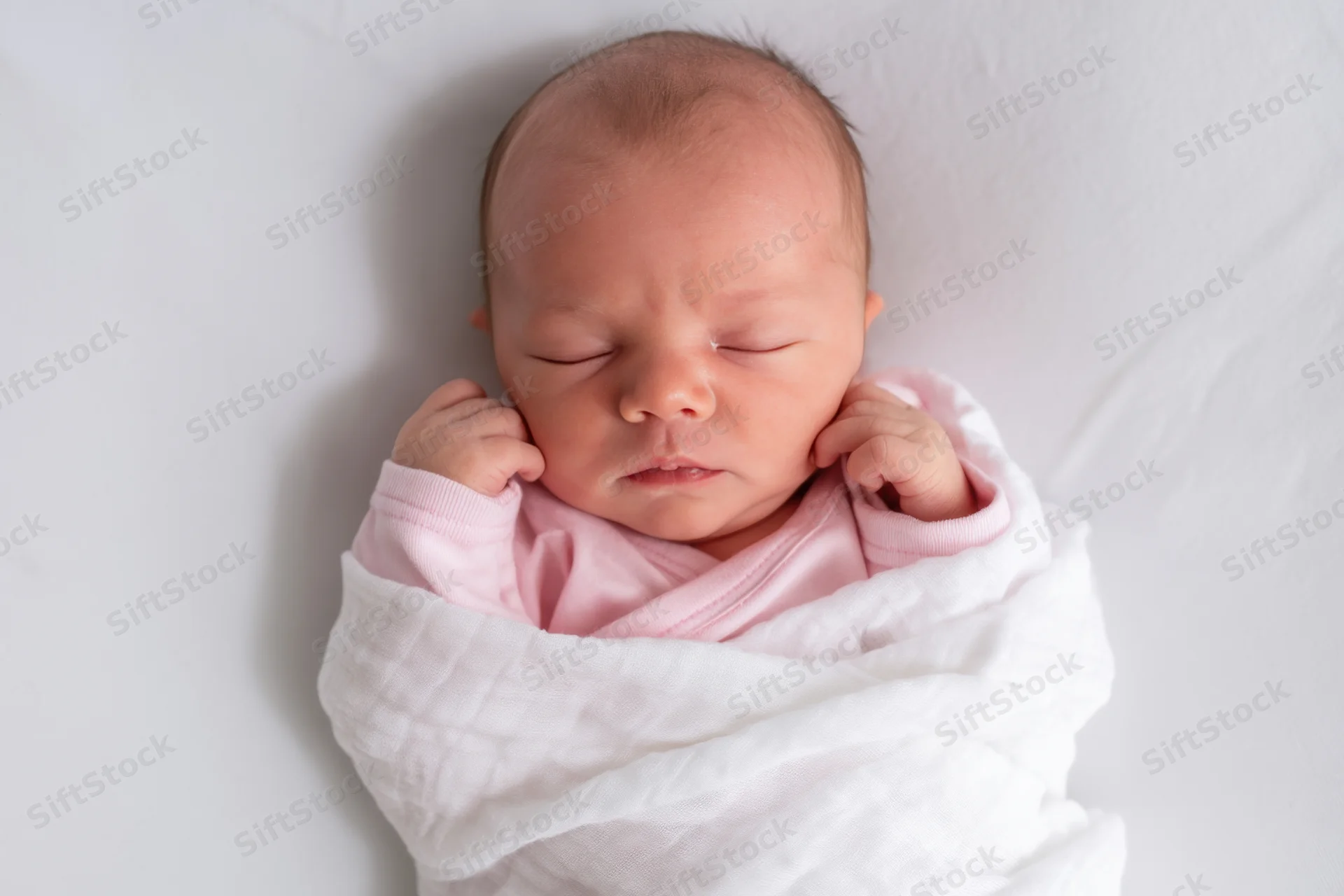 Newborn baby sleeping swaddled in white blanket with pink onesie, top view