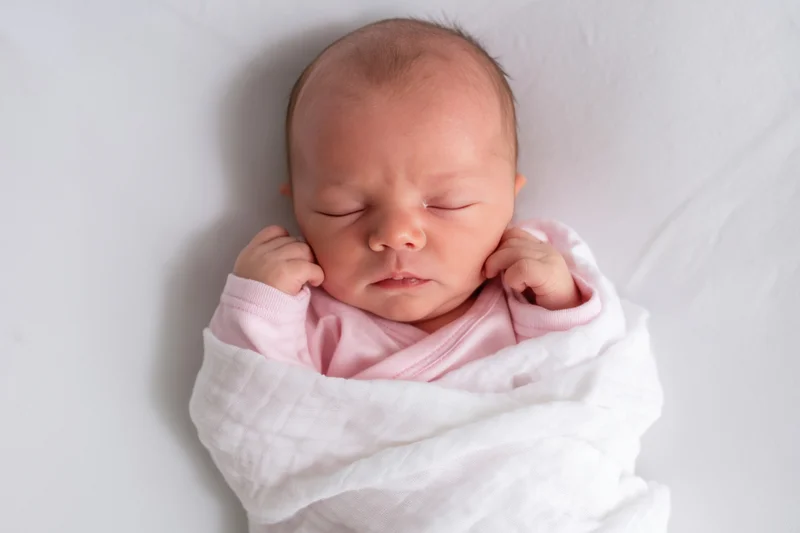 Newborn baby sleeping swaddled in white blanket with pink onesie, top view