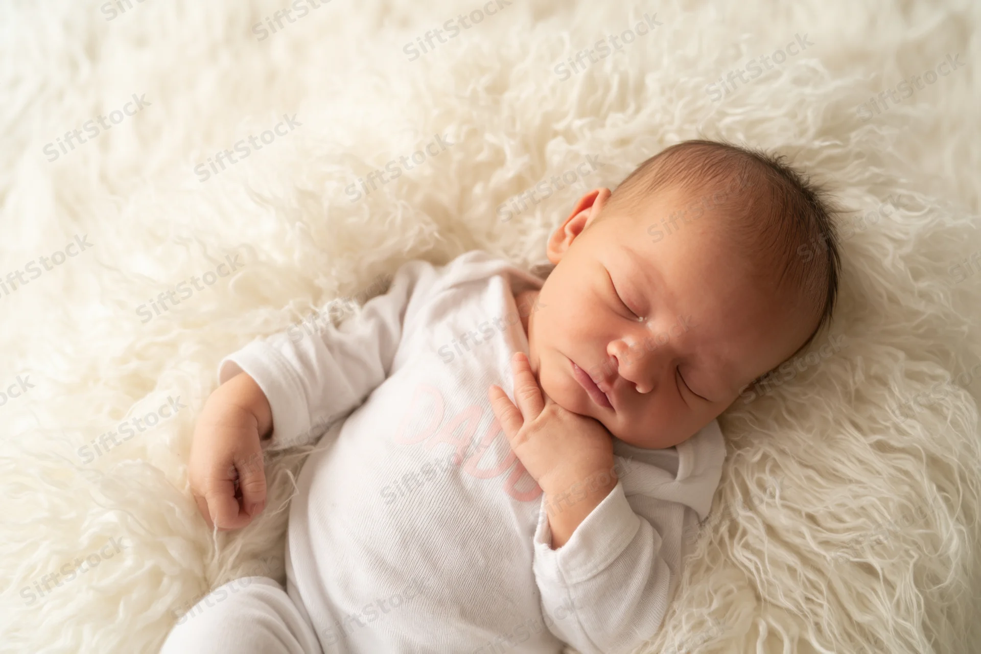 Newborn baby sleeping peacefully on a fluffy white fur blanket