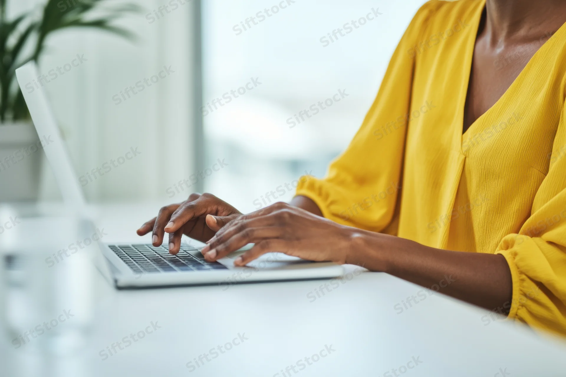 Woman typing on a silver laptop at a white desk in an office setting