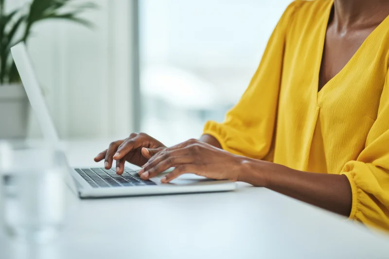Woman typing on a silver laptop at a white desk in an office setting
