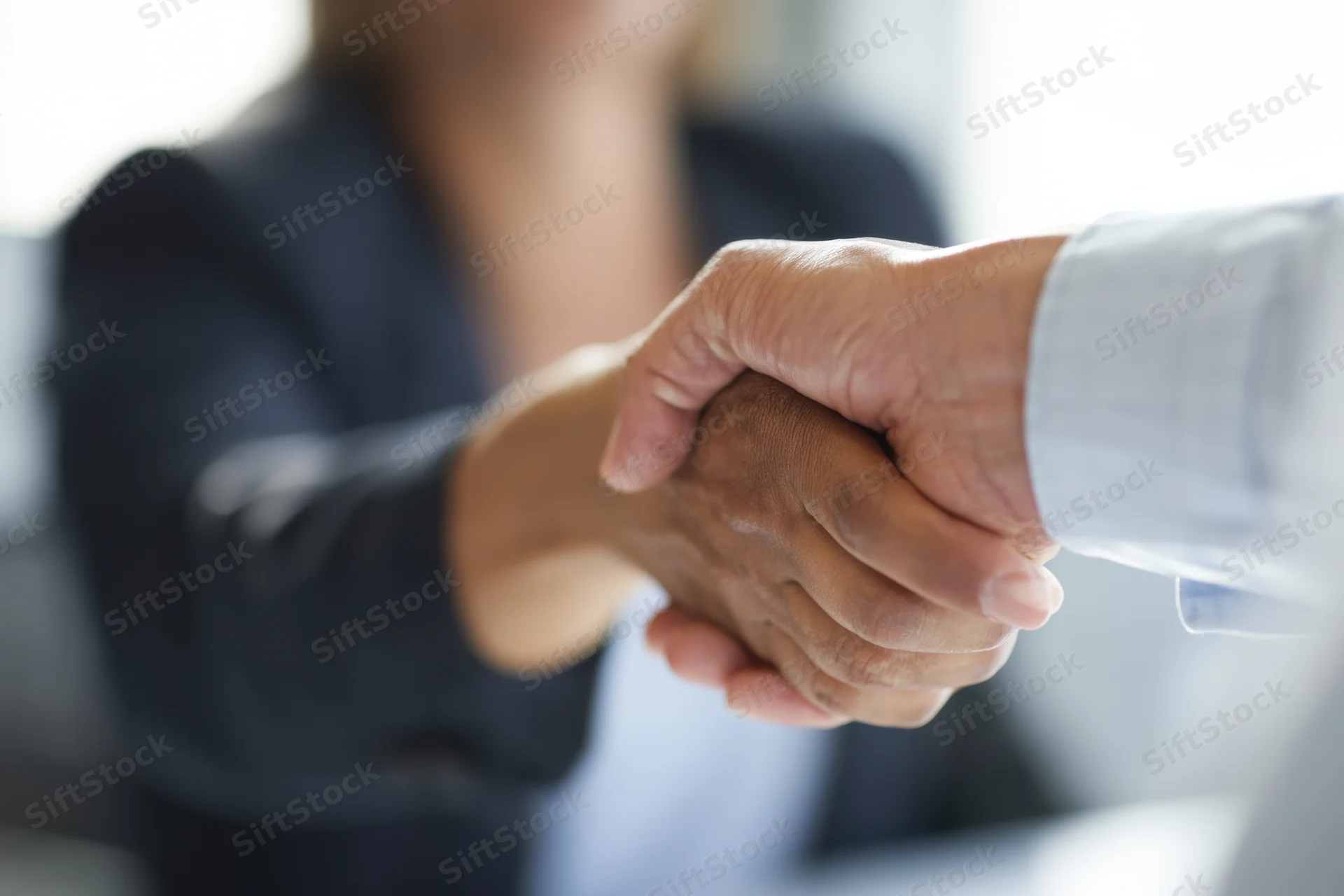 Close-up of a professional handshake between a woman in a suit and a man in a shirt in an office setting