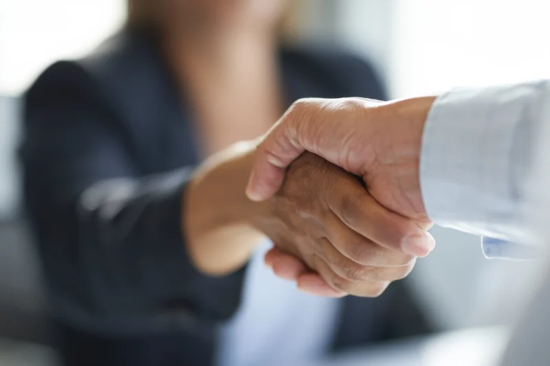 Close-up of a professional handshake between a woman in a suit and a man in a shirt in an office setting