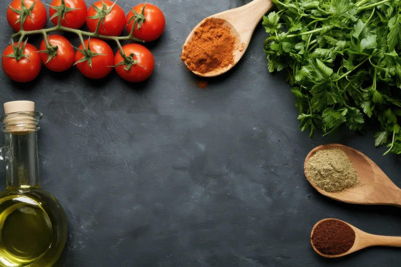 Fresh tomatoes on vine, parsley, olive oil, and spices in wooden spoons arranged on dark countertop