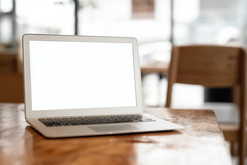 Silver laptop with blank white screen on wooden table in bright interior