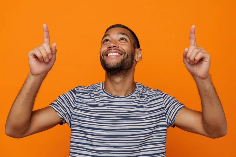 Smiling man pointing upward with both index fingers against bright orange background