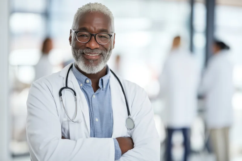 Smiling senior african male doctor with stethoscope and arms crossed in hospital setting