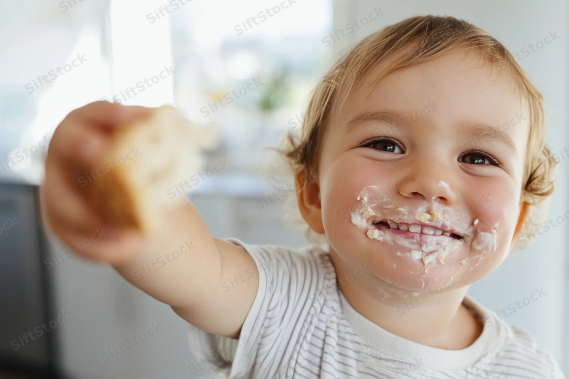 Smiling toddler with food smeared on face reaching forward in kitchen