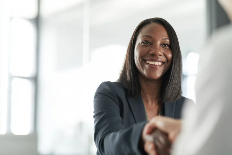Smiling woman in dark blazer shaking hands in bright office interior