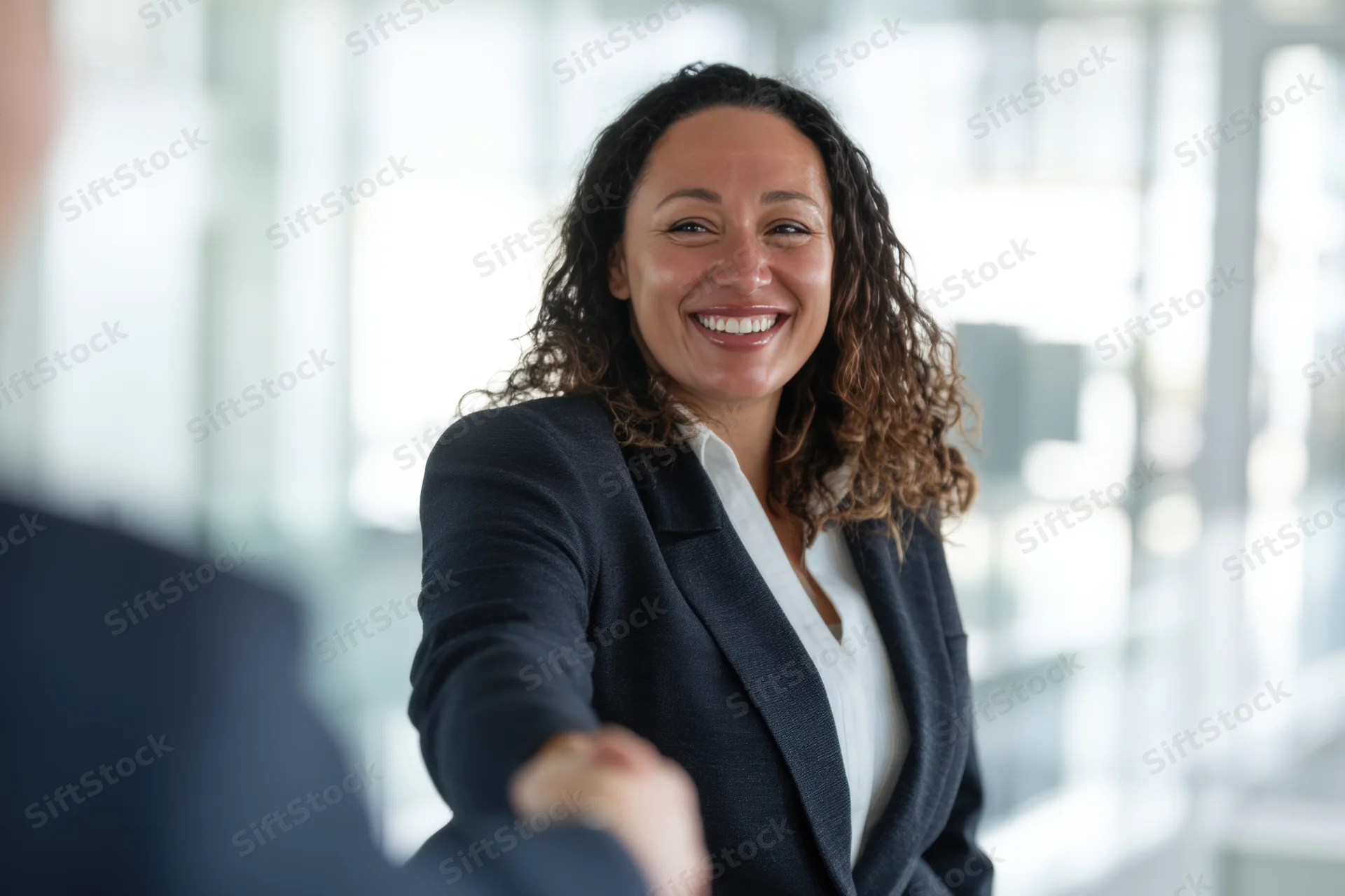 Woman in dark blazer smiling while shaking hands in office setting