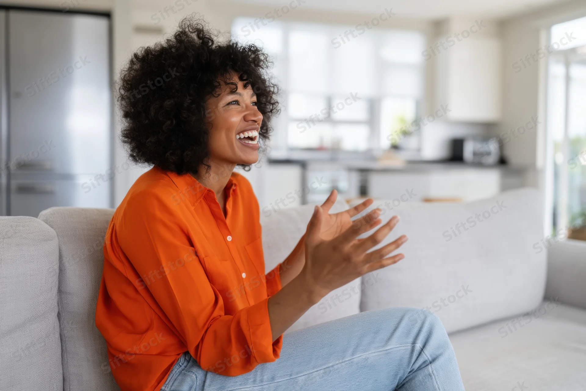 Woman laughing and gesturing while sitting on a couch in a modern living room