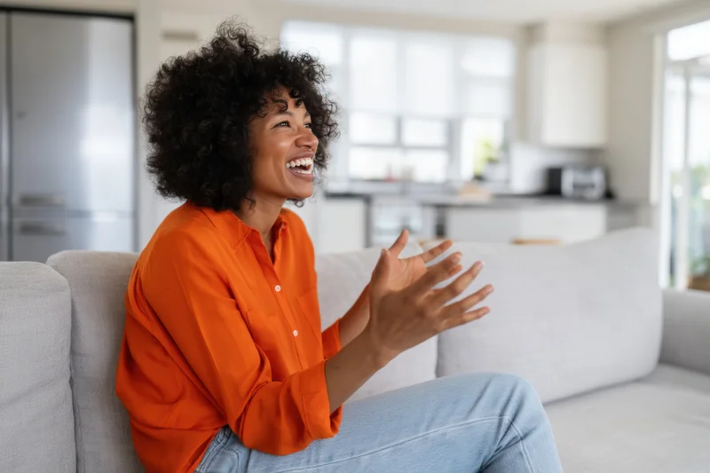 Woman laughing and gesturing while sitting on a couch in a modern living room