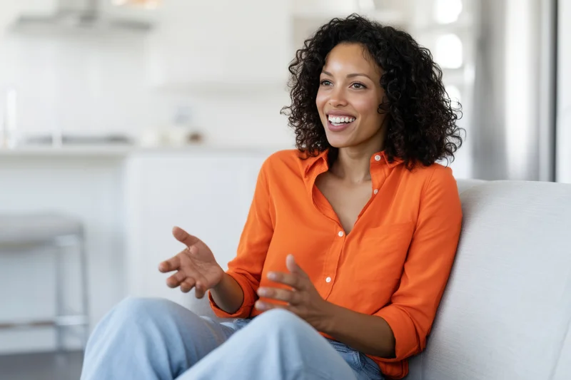 Woman smiling and gesturing while sitting on a couch in a modern living room