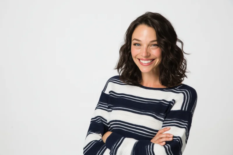 Smiling woman with arms crossed wearing a navy and white striped sweater in a studio setting
