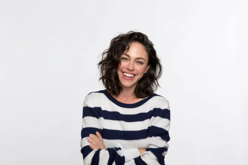 Smiling woman with arms crossed wearing a navy and white striped sweater in a studio setting