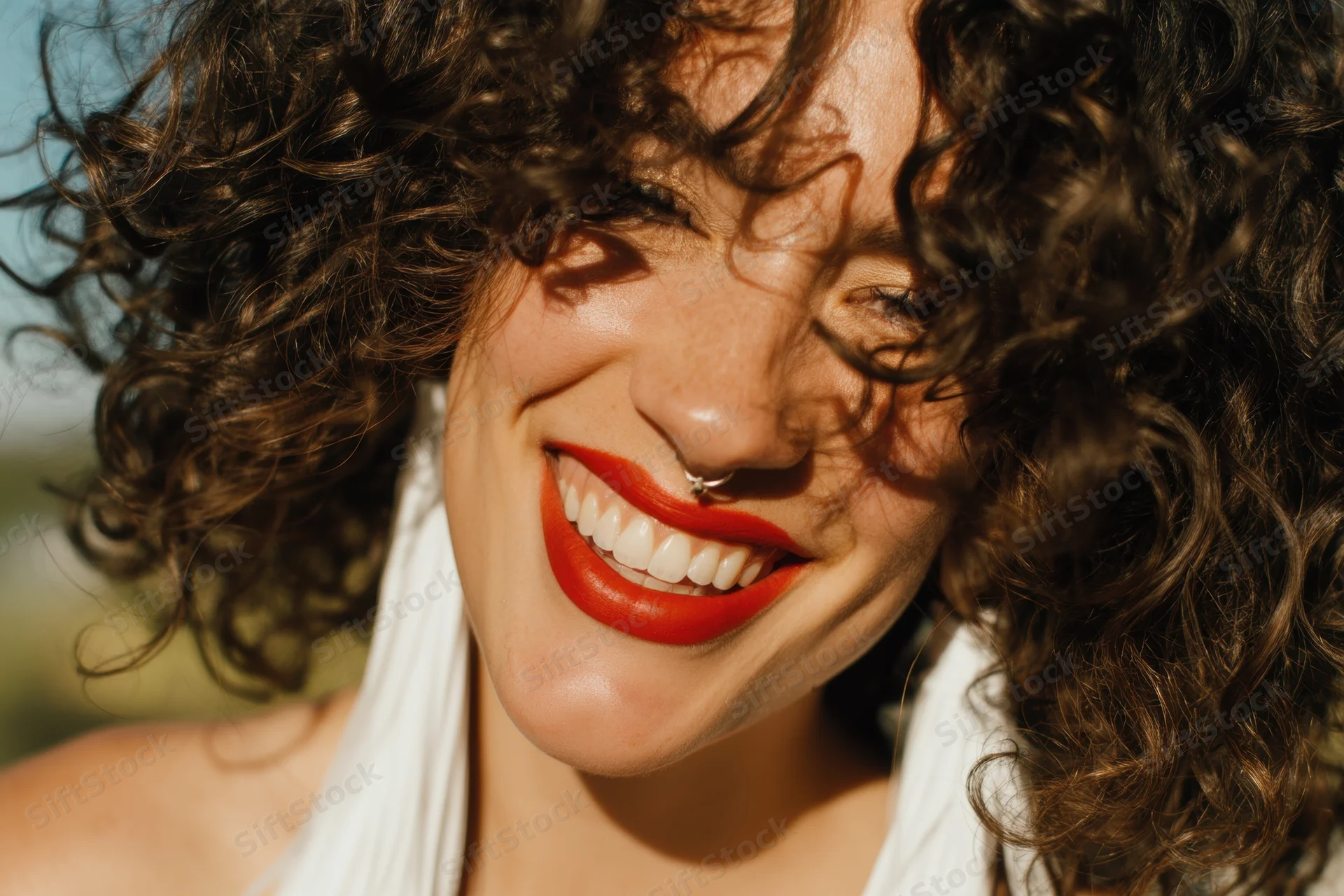 Smiling woman with voluminous curly hair and bright red lips outdoors in sunlight