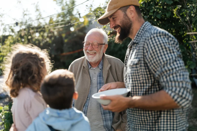 Senior man laughing with children and younger man in backyard garden gathering