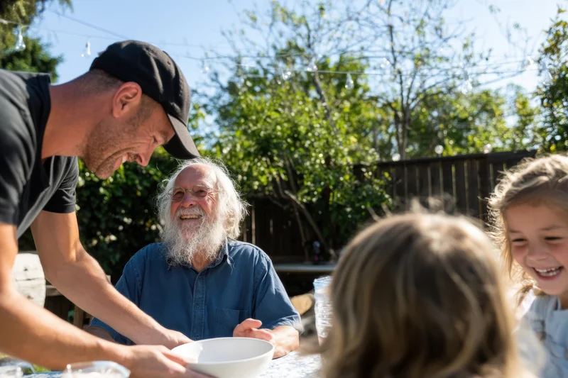 Elderly man with white beard smiling at children during backyard family gathering