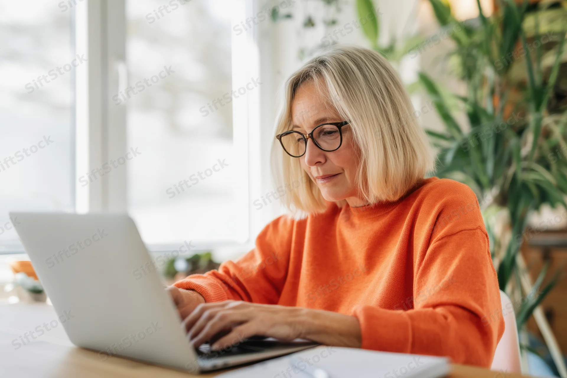 Woman typing on laptop at home office desk by window