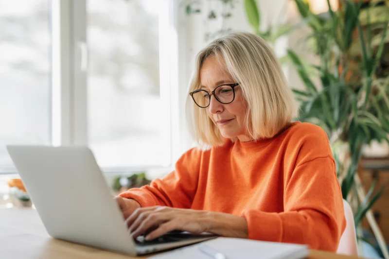 Woman typing on laptop at home office desk by window