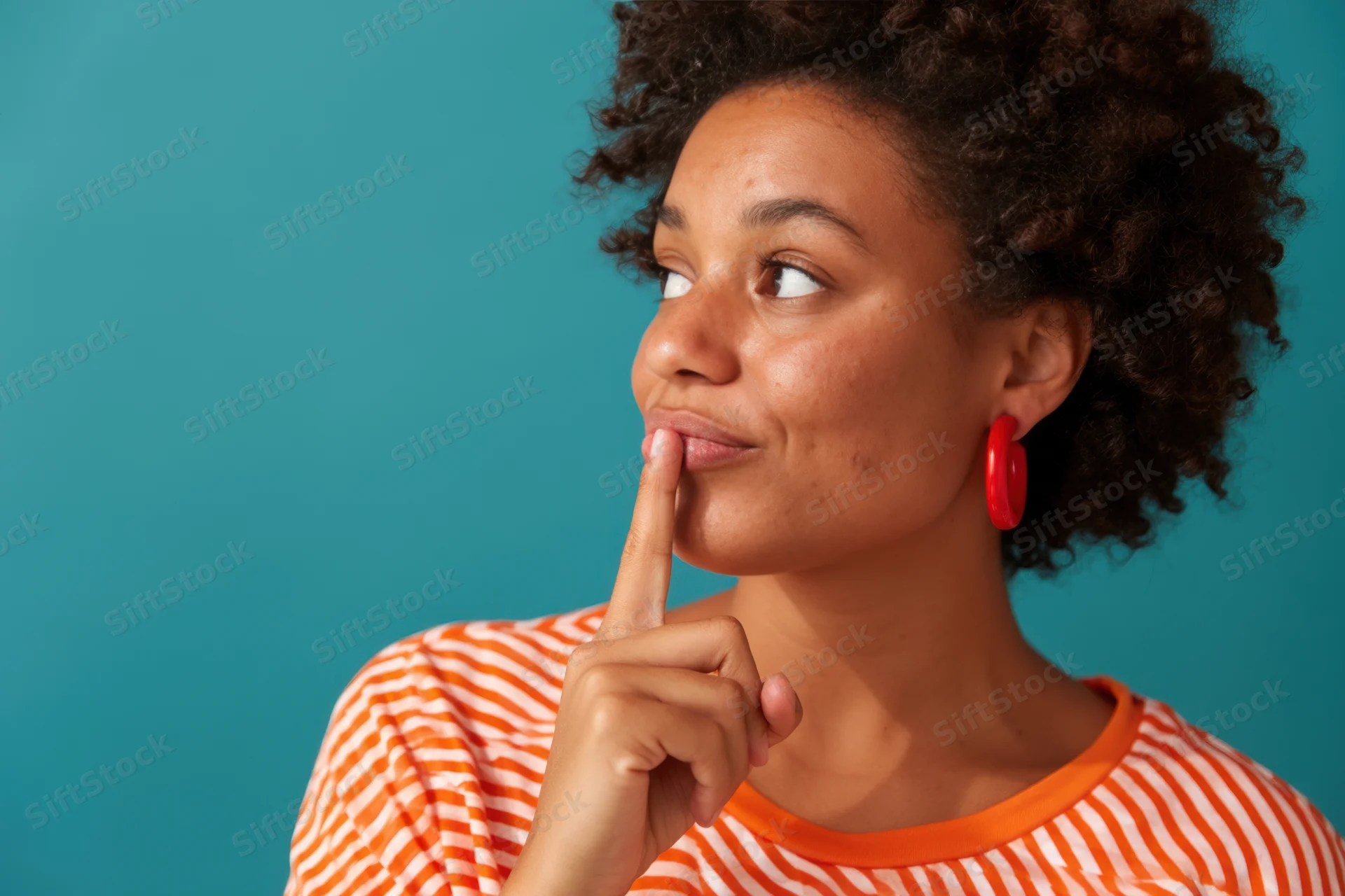 Young woman with curly hair touching her lips thoughtfully against a teal background